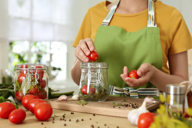 Photo of Woman putting tomatoes into pickling jar at table in kitchen, closeup