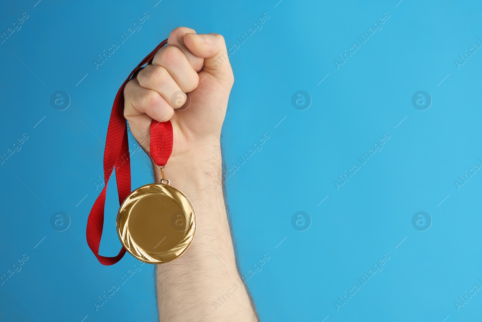 Photo of Man holding golden medal on blue background, closeup. Space for design