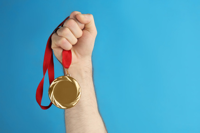 Man holding golden medal on blue background, closeup. Space for design