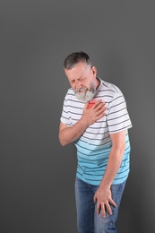 Mature man having heart attack on gray background