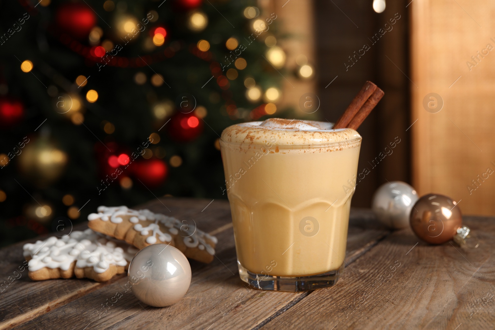 Photo of Tasty eggnog with cinnamon, cookies and Christmas baubles on wooden table against blurred festive lights. Space for text