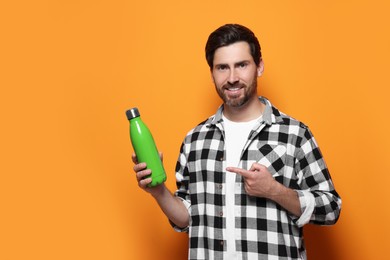 Man pointing on green thermo bottle against orange background. Space for text