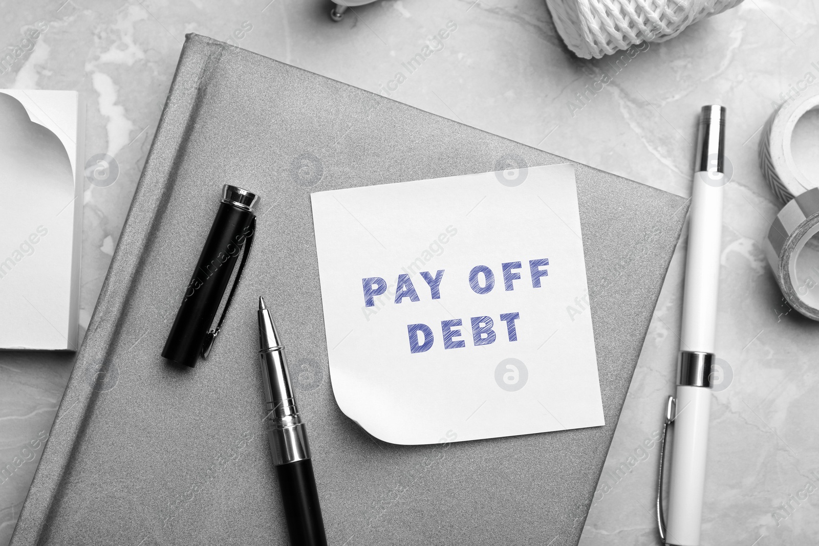 Image of Reminder note with phrase Pay Off Debt and stationery on grey marble table, flat lay