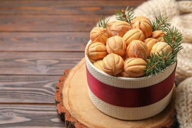 Photo of Bowl of delicious nut shaped cookies and fir tree branches on wooden table. Space for text