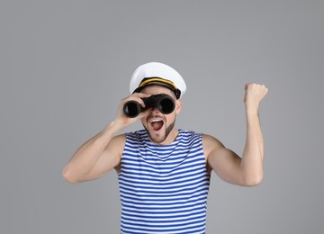 Photo of Happy sailor looking through binoculars on grey background