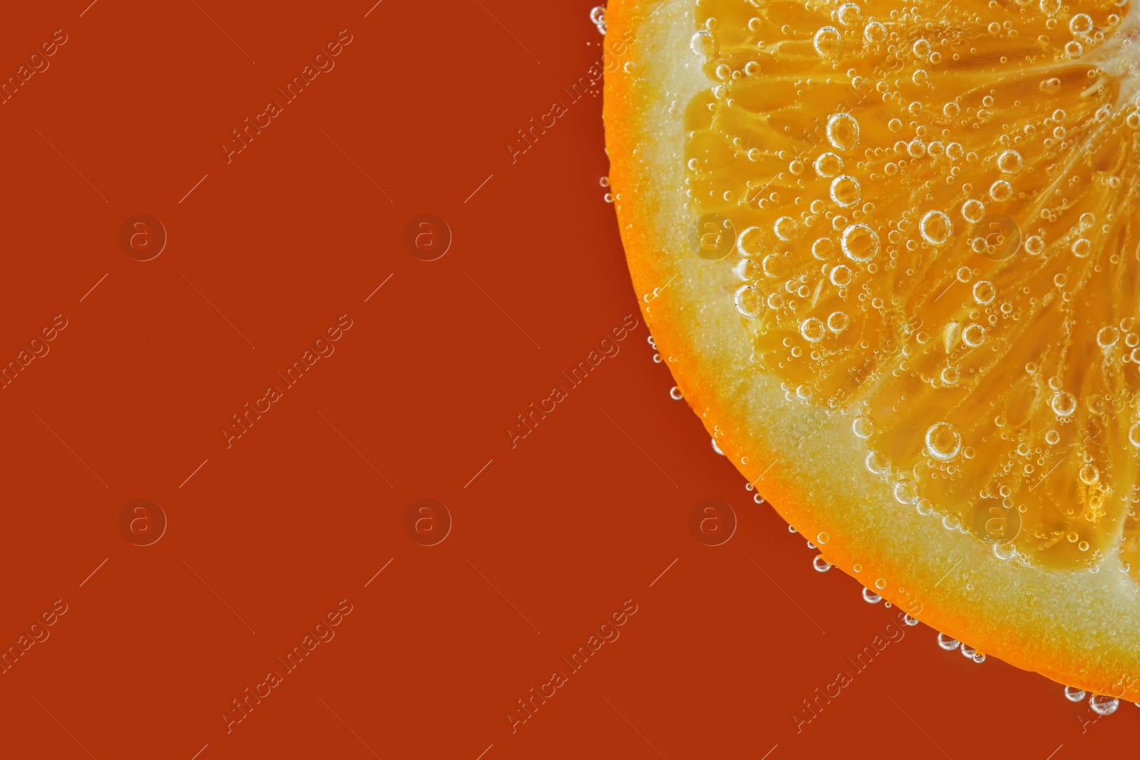 Photo of Fresh orange slice in sparkling water on red background, closeup. Space for text