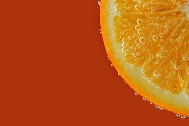 Photo of Fresh orange slice in sparkling water on red background, closeup. Space for text