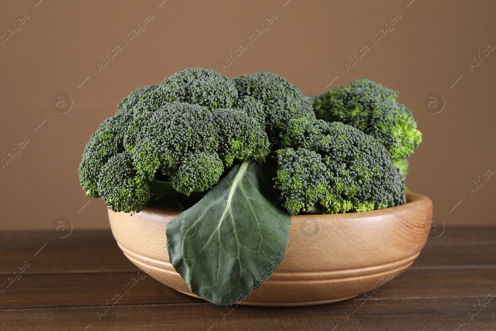 Photo of Bowl with fresh raw broccoli on wooden table, closeup