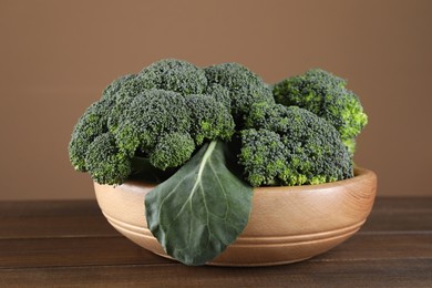 Bowl with fresh raw broccoli on wooden table, closeup