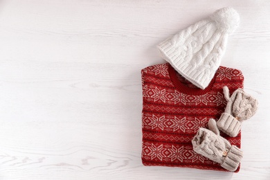 Mittens, hat and Christmas sweater with pattern on wooden background, top view. Space for text