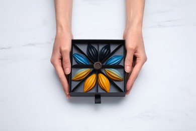 Photo of Woman holding box of delicious chocolate candies on white marble table, top view