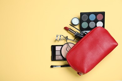 Cosmetic bag with makeup products and accessories on yellow background, flat lay. Space for text