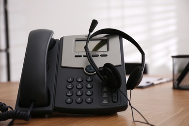 Photo of Desktop telephone and headset on wooden table in office. Hotline service