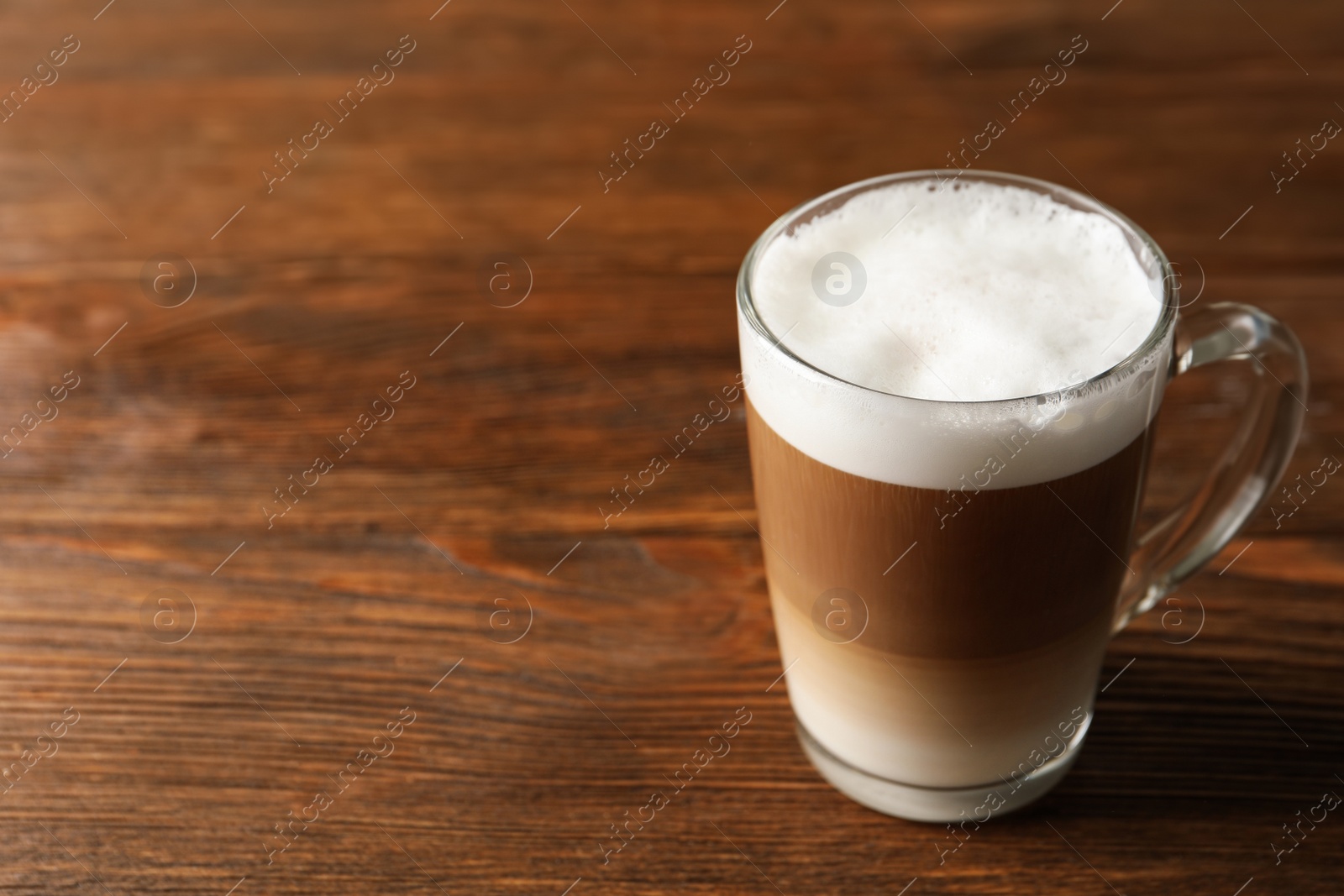 Photo of Glass cup of delicious layered coffee on wooden table, space for text