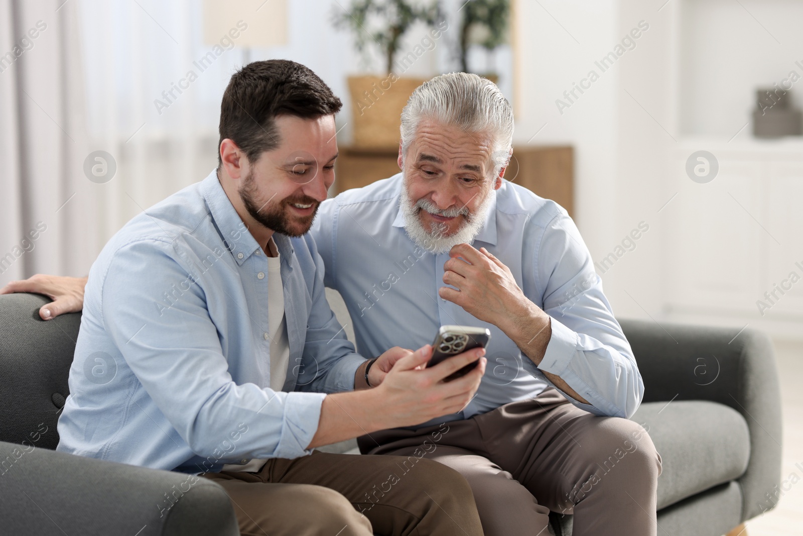 Photo of Happy son and his dad watching something on smartphone at home