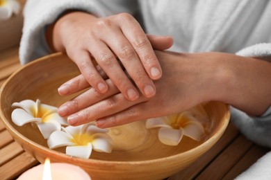 Woman soaking her hands in bowl of water and flowers at table, closeup. Spa treatment