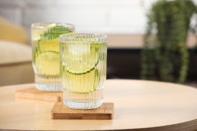 Glasses of lemonade and stylish cup coasters on wooden table in room. Space for text