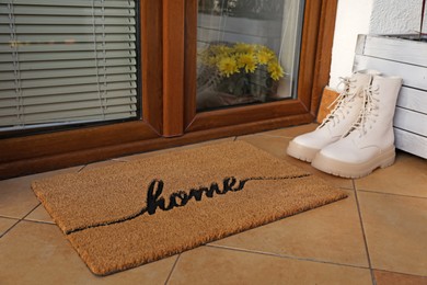Doormat with word Home and stylish boots near entrance outdoors