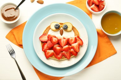 Photo of Creative serving for kids. Plate with cute owl made of pancakes, strawberries, cream, banana and almond on white wooden table, flat lay