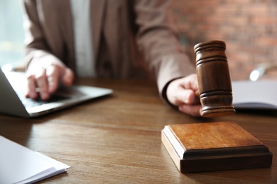 Photo of Judge with gavel at table in courtroom, closeup. Law and justice concept