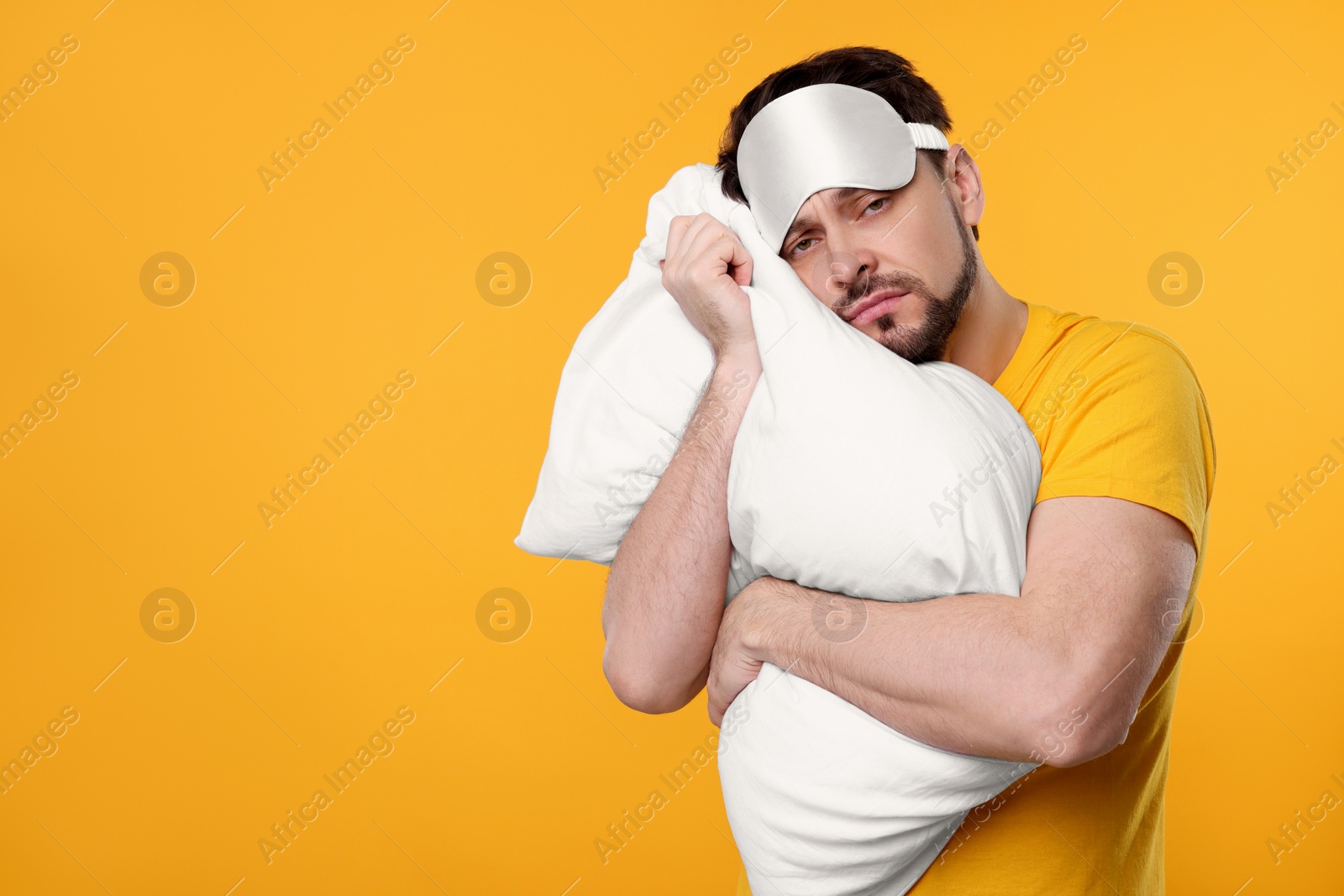 Photo of Tired man with sleep mask and pillow on yellow background, space for text. Insomnia problem