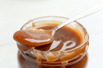 Photo of Jar and spoon with caramel sauce on white background, closeup