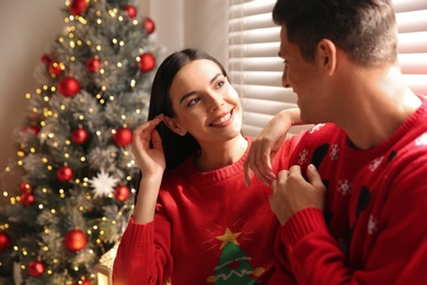 Happy couple in warm sweaters near Christmas tree indoors