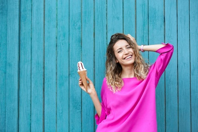 Photo of Happy young woman with delicious ice cream in waffle cone near wooden wall. Space for text