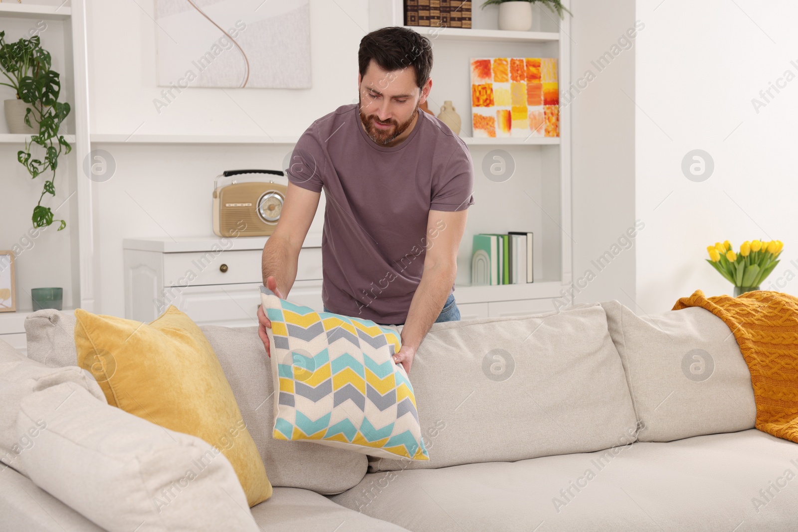 Photo of Spring cleaning. Man putting pillow on sofa in living room