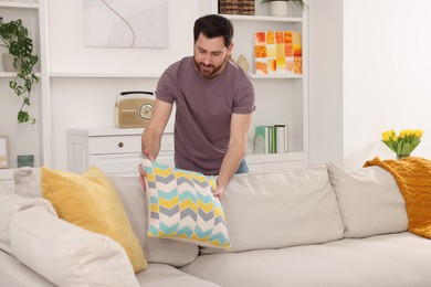 Spring cleaning. Man putting pillow on sofa in living room