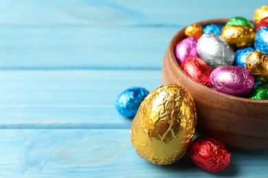 Photo of Chocolate eggs wrapped in colorful foil on light blue wooden table. Space for text