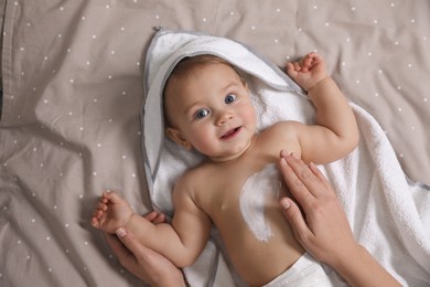 Photo of Mother applying moisturizing cream onto her little baby's skin on bed, closeup