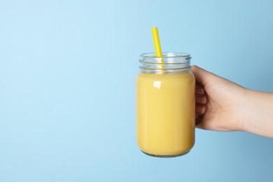 Woman holding mason jar with tasty smoothie and straw on light blue background, closeup. Space for text