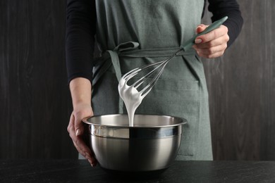 Woman making whipped cream with whisk at black table, closeup