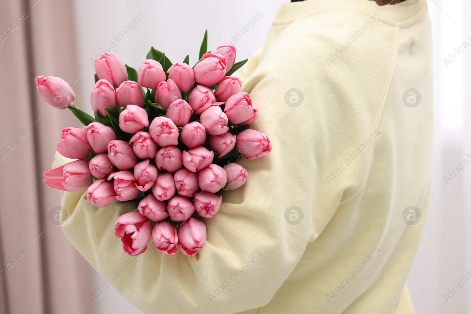 Photo of Woman holding bouquet of pink tulips indoors, closeup