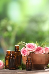 Bottles with essential oils, roses and rosemary on wooden table against blurred green background. Space for text