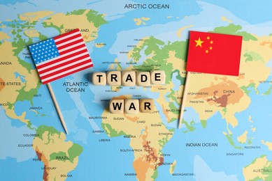 Photo of Phrase Trade war made with wooden cubes near USA and China flags on world map, flat lay
