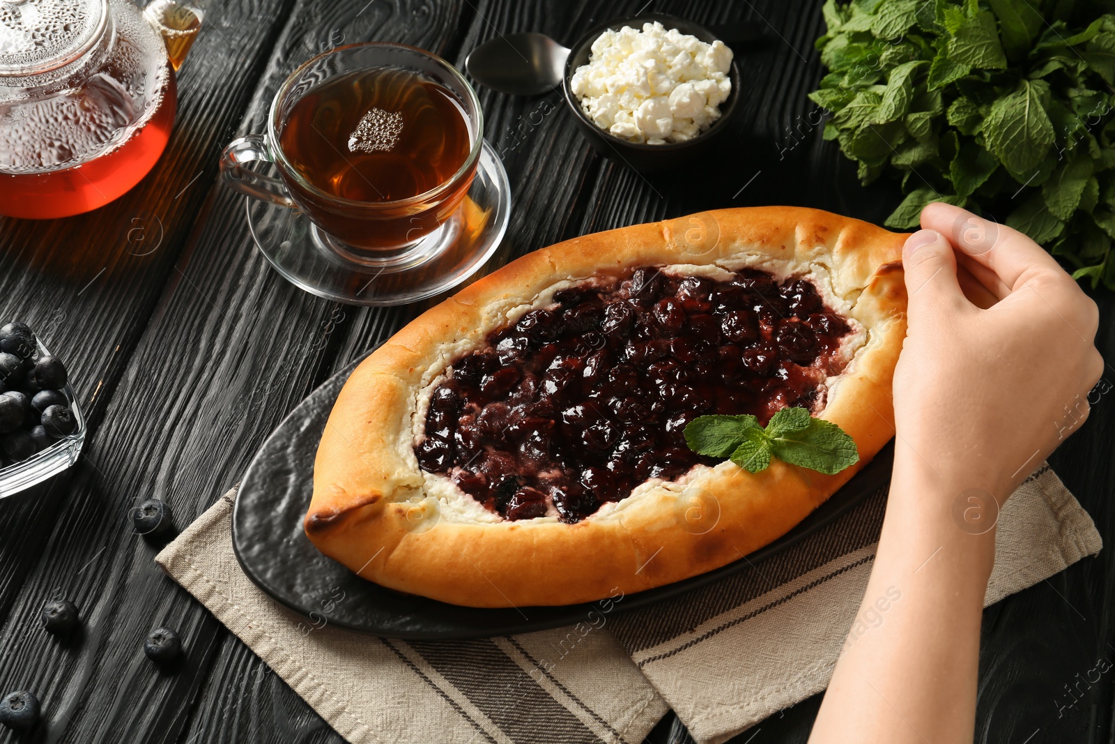 Photo of Woman eating delicious sweet cottage cheese pastry with cherry jam at black wooden table, above view