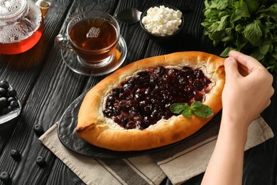 Photo of Woman eating delicious sweet cottage cheese pastry with cherry jam at black wooden table, above view