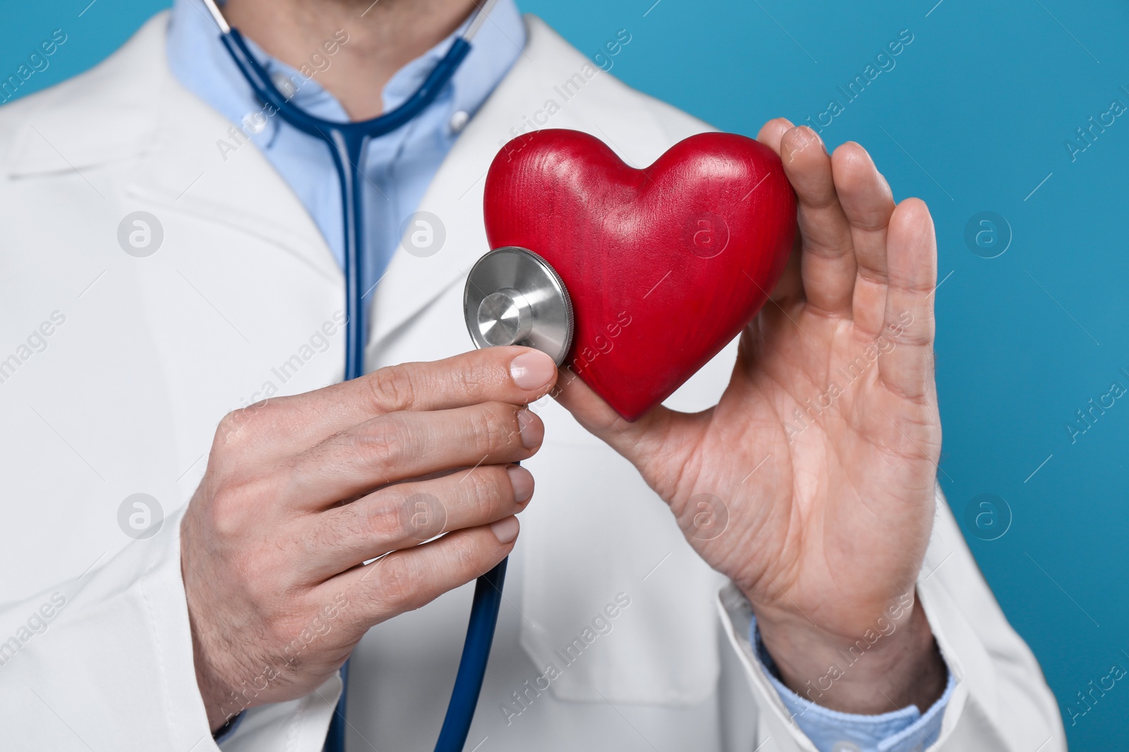 Photo of Doctor with stethoscope and red heart on light blue background, closeup. Cardiology concept