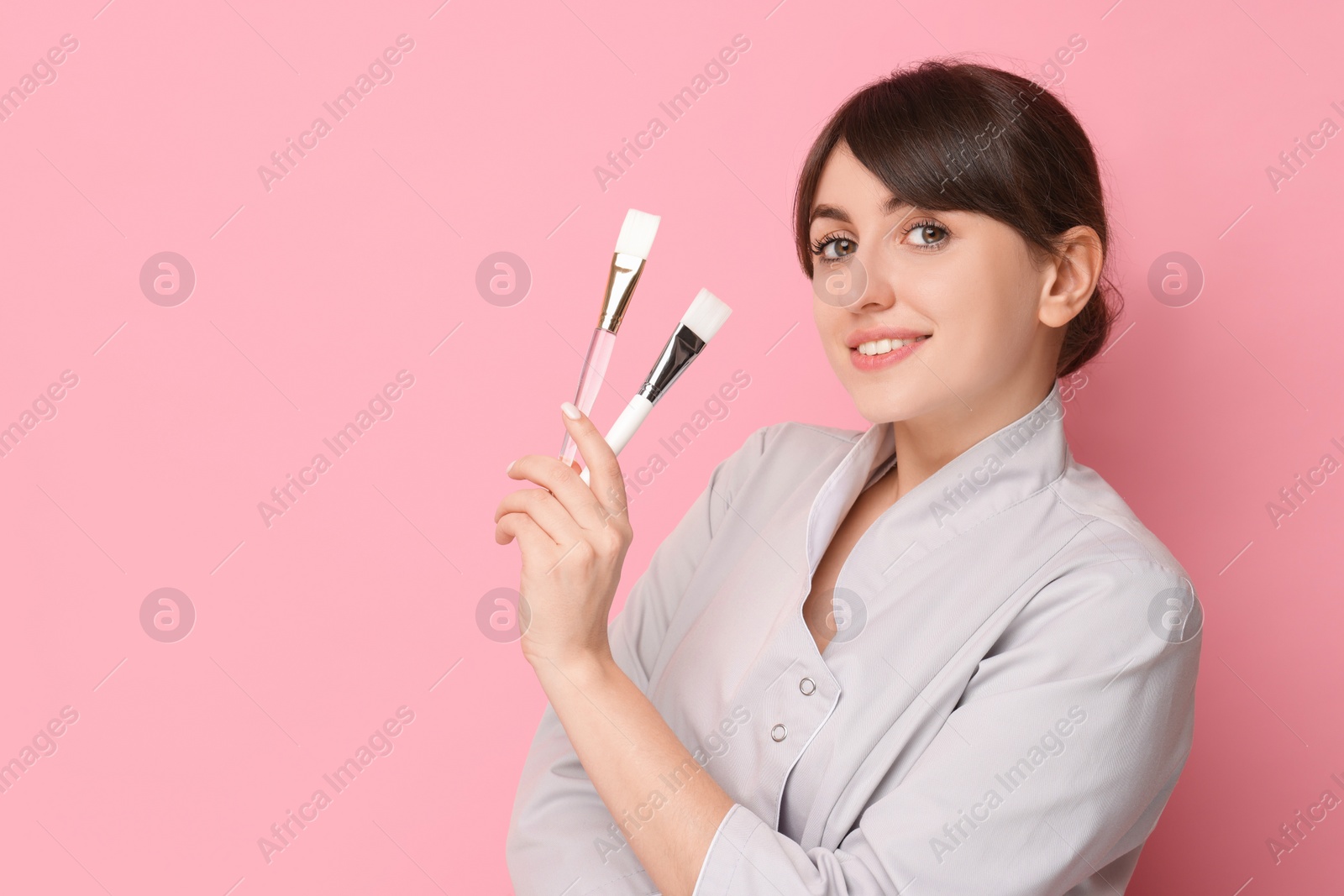 Photo of Cosmetologist with cosmetic brushes on pink background, space for text