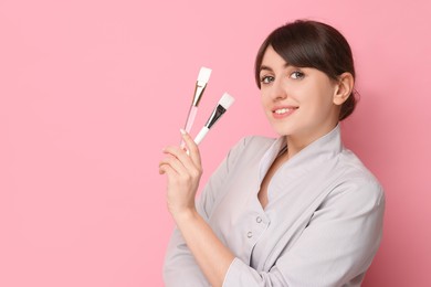 Cosmetologist with cosmetic brushes on pink background, space for text