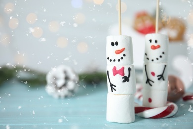Photo of Funny snowmen made of marshmallows on light blue wooden table, closeup. Space for text