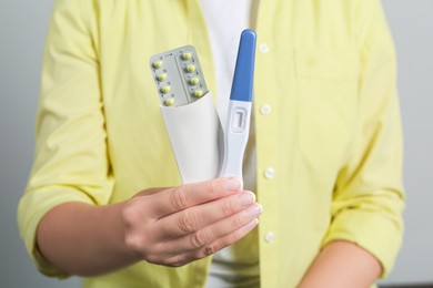 Woman holding birth control pills pregnancy test on grey background, closeup