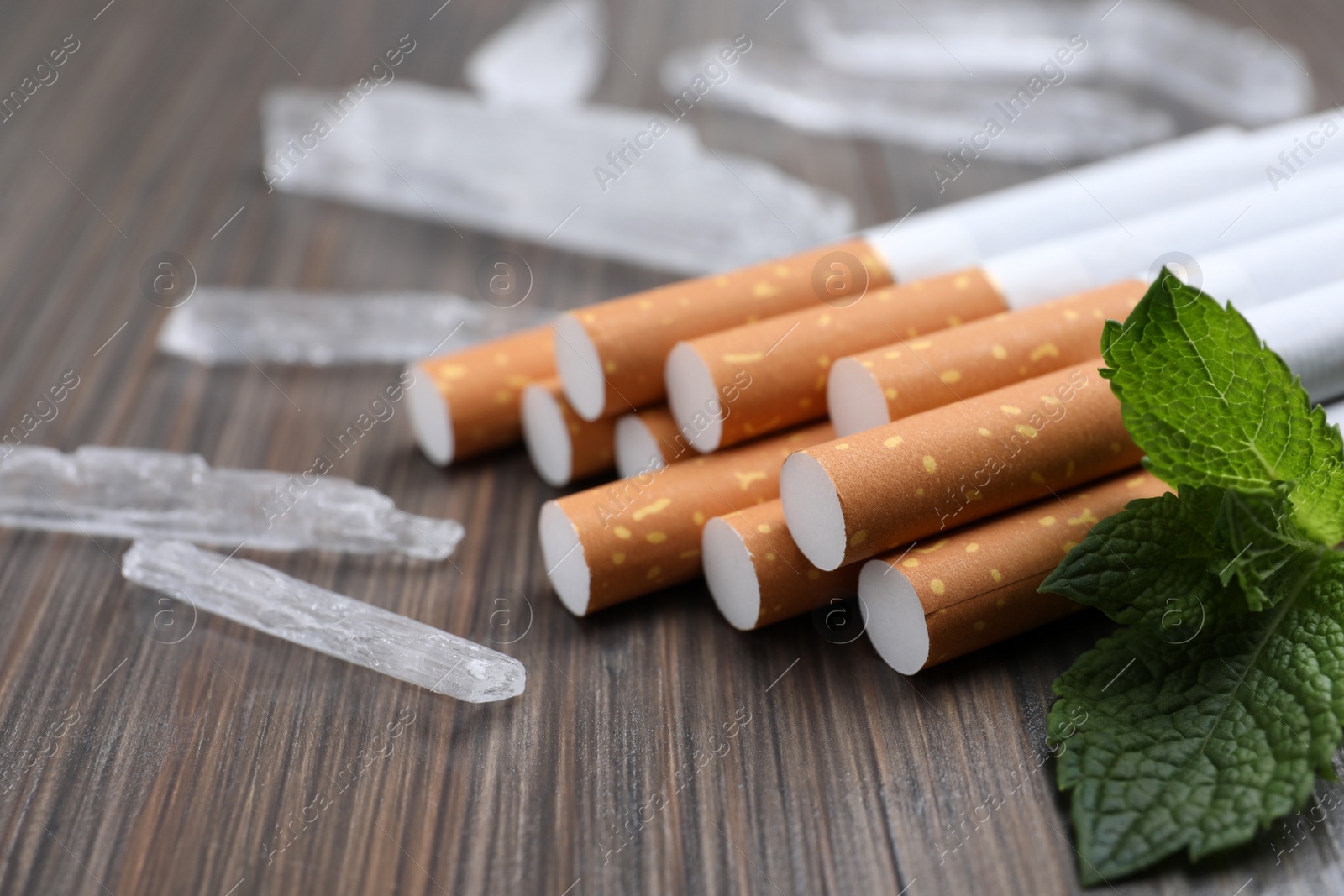 Photo of Cigarettes, menthol crystals and mint on wooden table, closeup