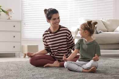 Young mother and her daughter meditating together at home