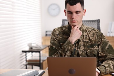 Photo of Military service. Young soldier working with laptop at table in office, space for text