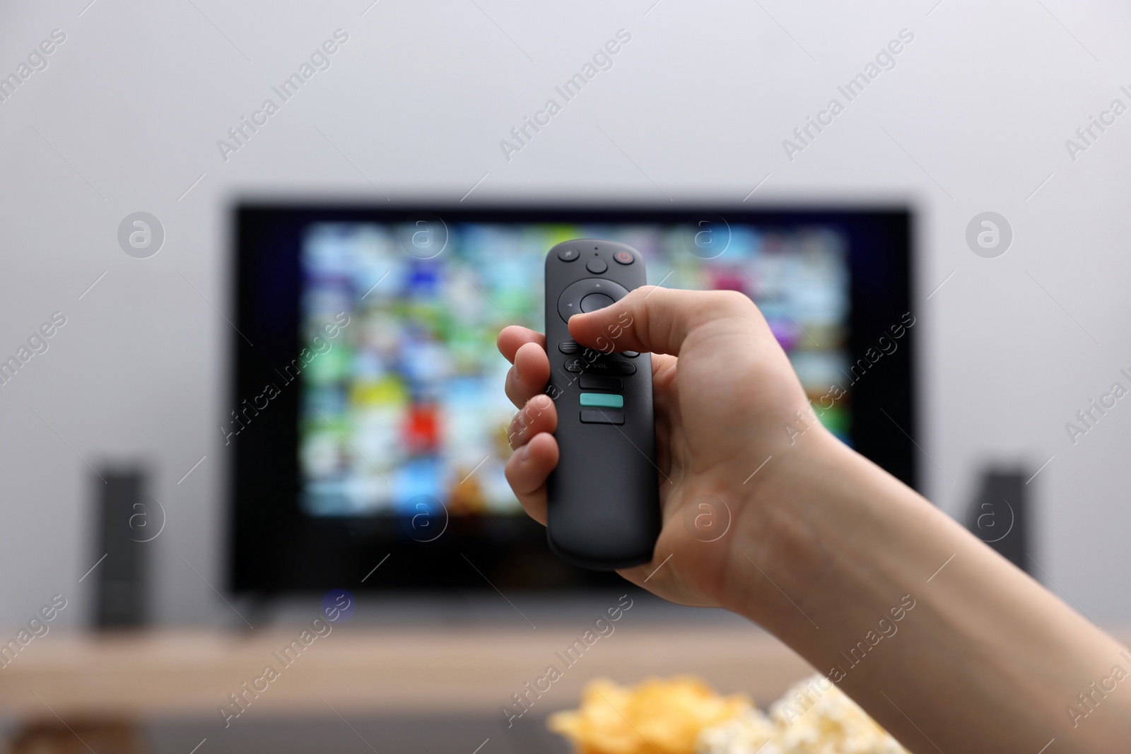 Photo of Woman switching channels on TV set with remote control at home, closeup