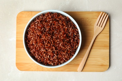 Photo of Bowl with delicious cooked brown rice on white marble table, top view