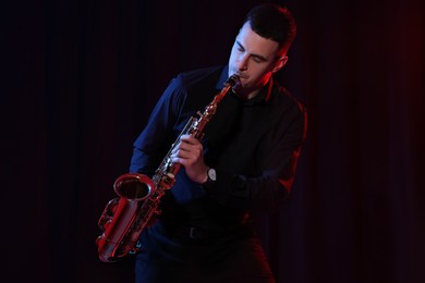 Photo of Young man playing saxophone on dark background